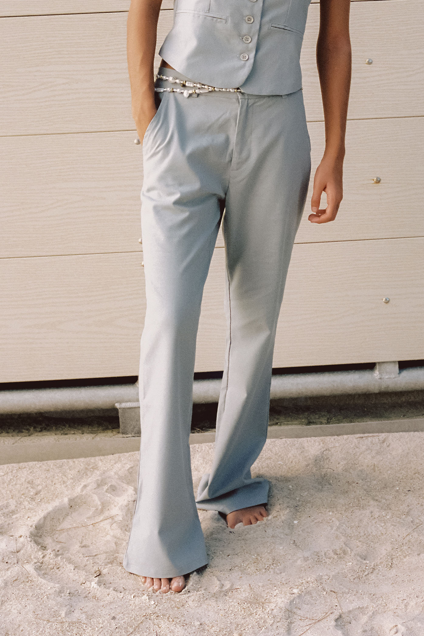 A zoomed-in detail of a model wearing the "Cleo Grey Pants" of the summer 23/24 collection in a beach in Costa Rica